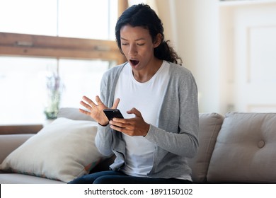 Confused Young African Ethnicity Woman Looking On Cellphone Screen With Opened Mouth, Feeling Disappointed With Broken Electronic Device Or Reading Unexpected Bad News In Sms Notification At Home.