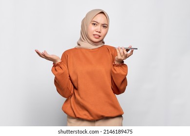 Confused young Asian woman in orange shirt using the voice assistant on mobile phone isolated over white background - Powered by Shutterstock