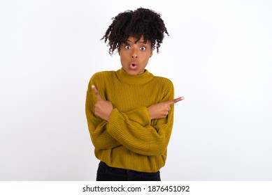 Confused Young beautiful African American woman wearing knitted sweater against white wall,  chooses between two ways, points at both sides with crossed hands, feels doubt. Need your advice. - Shutterstock ID 1876451092
