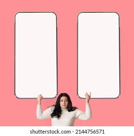 Confused Young Chubby Brunette Lady Showing Two Huge Cellphones With White Empty Displays For Advertisement, Making Choice Between Exciting Deals Over Pink Studio Background, Mockup