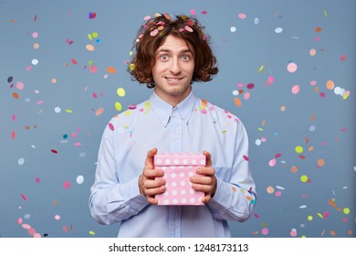 Confused Young Guy Keeps A Gift Box, Expression On His Face Puzzled, Bit His Lower Lip As If Something Had Forgotten Or Did Not Come Up With A Greeting For The Birthday Boy.