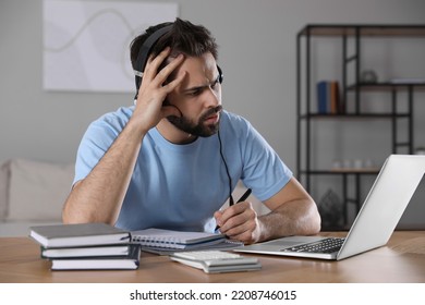 Confused Young Man Watching Webinar At Table In Room