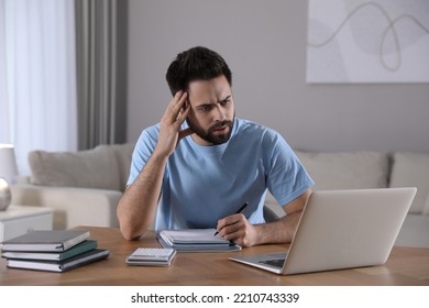 Confused Young Man Watching Webinar At Table In Room