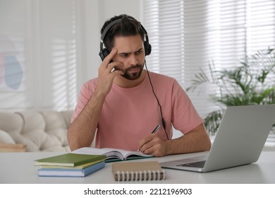 Confused Young Man Watching Webinar At Table In Room