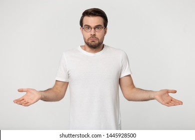 Confused young man wearing white t-shirt glasses being in perplexity, guy shrugged his shoulders look at camera feel puzzled isolated on gray studio background ambiguous situation, I dont know concept