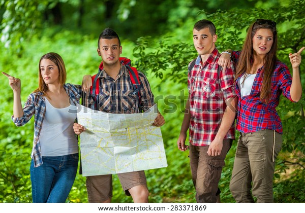 Confused young men with map looking at camera and confident young women showing them directions in the forest