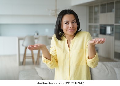 Confused young woman feels perplexity shrugging shoulders, raised palms, looking at camera at home. Puzzled unsure female homeowner housewife doesn't know answer. Dilemma, difficult choice.