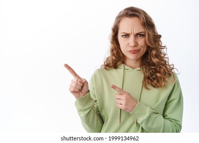 Confused Young Woman Frowning, Judging, Smirk And Look Upset And Displeased, Pointing At Upper Left Corner Promotional Text, Accuse Someone, White Background