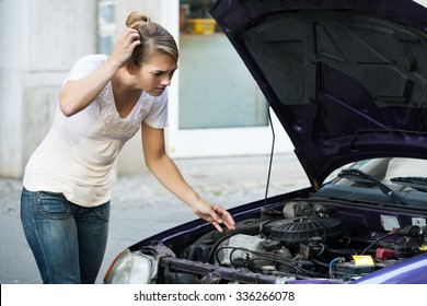 Confused Young Woman Looking At Broken Down Car Engine On Street