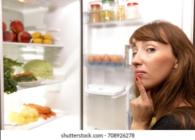 Confused Young Woman Looking In Fridge At Kitchen