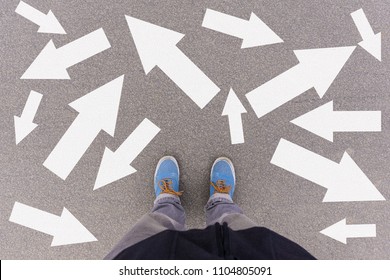Confusing direction arrows on asphalt ground, feet and shoes on floor, personal orientation concept - Shutterstock ID 1104805091