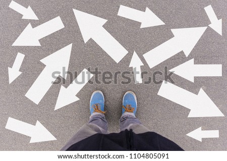 Confusing direction arrows on asphalt ground, feet and shoes on floor, personal orientation concept