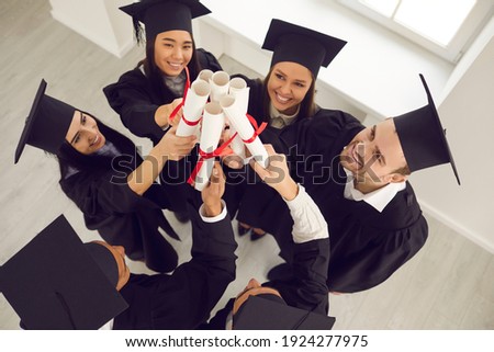 Congrats, grad. Happy successful college students celebrating graduation. High angle of smiling university graduates in traditional academic caps standing in circle, holding diplomas and joining hands