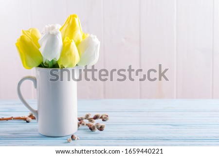 Congrats post card with fresh spring tulips flowers in a cup and fresh willow twigs on a light blue wooden table.