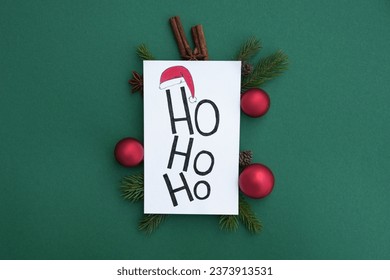 Congratulation  white postcard with inscription ho ho ho. Fir branch, decorations and Christmas spices on green background. Xmas or New Year greeting card template. Winter holiday theme. Flat lay.