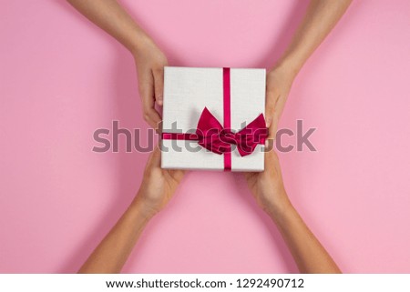 Congratulations background. Top view of two persons hands giving and receiving a present gift box with ribbon on pink background. Top view. Present for birthday, valentine day, Christmas, New Year.