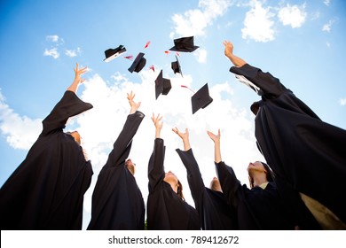 Congratulations! Low angle view of happy group of six young cheerful graduates in black gowns, throwing up their head wear in the air and celebrating, in blue summer sky, laughing, enjoying