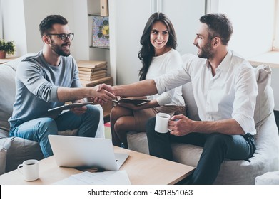 Congratulations! Three Young Cheerful Business People Sitting Together At The Desk While Men Shaking Hands 