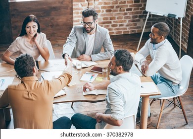 Congratulations with your promotion! Top view of two men shaking hands and smiling while their coworkers sitting at the table in office - Shutterstock ID 370382978