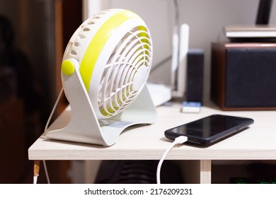 Connected Desk Fan And A Black Smart Phone On Charging. Home Nesting Concept With Power Consumption