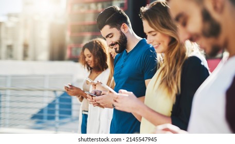 Connected Is The Only Way To Go. Cropped Shot Of A Handsome Young Man Sending A Text Message While Standing Outside With A Group Of Friends.