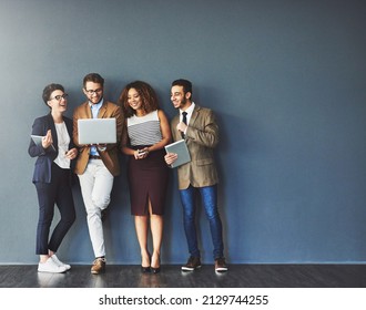 The connected team is an efficient team. Studio shot of a group of businesspeople using wireless technology together while standing in line against a gray background. - Shutterstock ID 2129744255