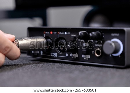 Connecting an XLR microphone cable to a compact black audio interface, featuring input gain controls, critical for home studio and professional sound capture
