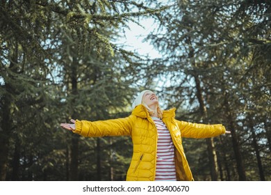 Connection with nature. Woman traveler in yellow jacket breathing clean air in nature forest. Happy girl with open arms in happiness. Fresh outdoor woods, wellness healthy lifestyle concept.