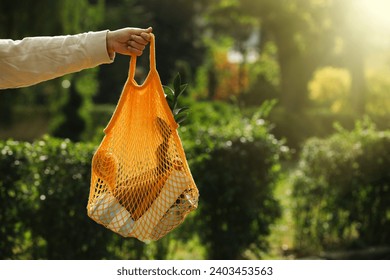 Conscious consumption. Woman with net bag of eco friendly products outdoors, closeup. Space for text - Powered by Shutterstock