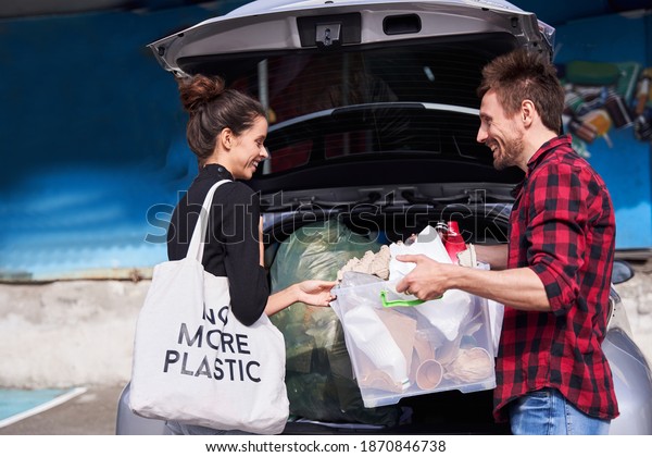 Conscious family. Active woman with eco bag and her\
unshaven smiling husband came to the garbage sorting factory by\
their electro car. Stock\
photo