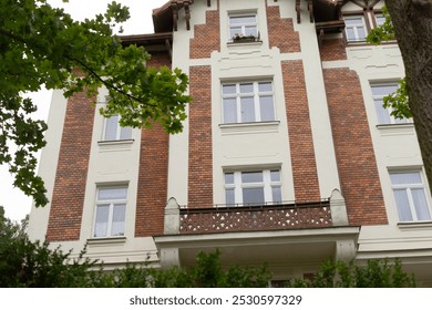 A considerable and expansive brick building featuring a balcony and a lovely tree positioned right in front of it