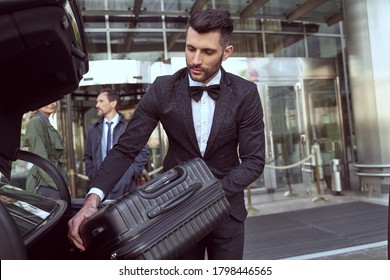 Considerate Hotel Porter Wearing Uniform Handling A Piece Of Luggage And Placing It Into A Car Trunk