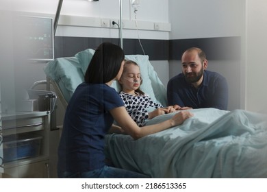 Considerate Parents Sitting Beside Hospitalized Sick Little Daughter Inside Children Healthcare Facility Room. Loving Family Comforting Under Treatment Sleeping Ill Kid In Hospital Pediatric Ward.