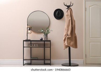 Console table, clothes rack and mirror on beige wall in hallway. Interior design
