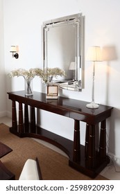 Console table and rectangular mirror in modern interior. There is vase with orchids and lamp on table. Jewelry box with decorative glass ball inside. Modern interior.