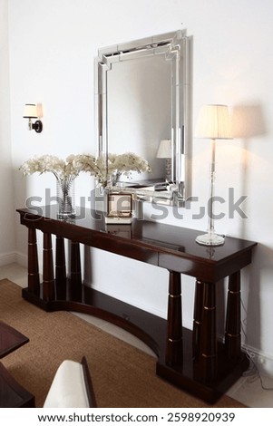 Console table and rectangular mirror in modern interior. There is vase with orchids and lamp on table. Jewelry box with decorative glass ball inside. Modern interior.