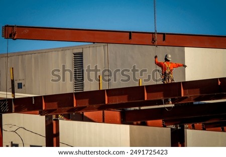 A consruction worker directing placement of a large steel beam that is atttached to a crane 