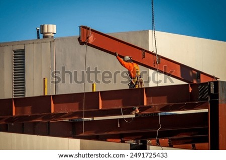 A consruction worker directing placement of a large steel beam that is atttached to a crane 