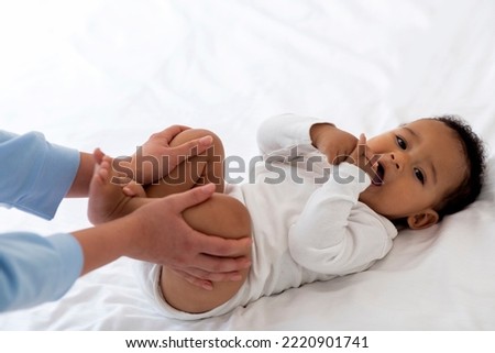 Constipation In Babies. Closeup Shot Of Caring Mother Doing Gymnastics With Cute Black Infant Child Lying On Bed, Unrecognizable Mom Making Massage To Little African American Boy To Relieve Gases