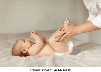 Constipation in babies. Mother doing gymnastics with her newborn child to relieve gases, moving kid's legs, infant lying on bed, side view, copy space - Shutterstock ID 2352983839