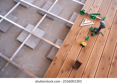 Constructing a wooden deck involves measuring and placing tools carefully alongside materials on a flat surface.