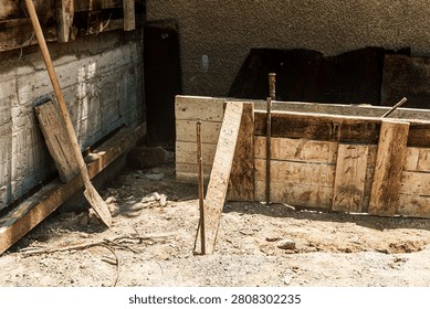Construction area featuring wooden forms and tools on the ground, with a partially completed concrete structure and dirt visible in the background