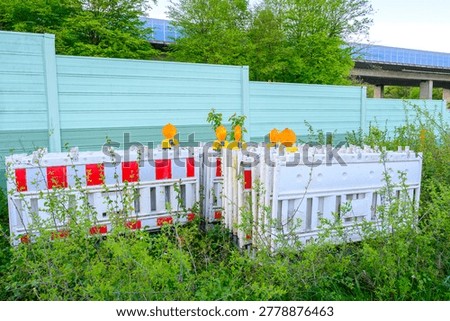Construction barriers and warning lights stacked near a highway sound barrier