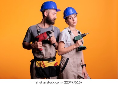 Construction builders posing with drilling tools in studio, holding electric power drills for renovation work. Team of contractors working together on refurbishment project, using nail guns.