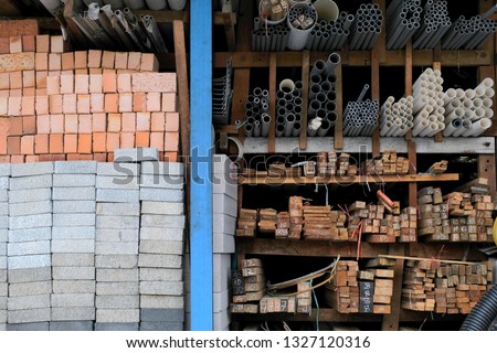 Construction building materials and industrial supplies such as bricks, woods and pipes stacked and arranged for sale at a hardware store front.