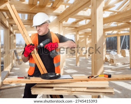 Construction carpentry, Timber frame assembly. Carpenter drills wooden beams at a construction site, preparing structural elements for building installation and house framing.