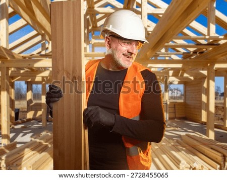 Construction carpentry, timber framing. Builder in hard hat and safety vest installs wooden beams at house frame site, performing structural assembly and residential construction work.