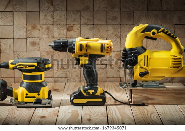 construction carpentry tools\
electric corded jigsaw cordless drill and wood sander on wooden\
background