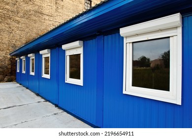 Construction change house fragment. Temporary blue building for builders. Portable blue change house. Long construction building next to brick wall. Concept of selling change houses for builders
