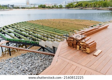 The construction of the city embankment, the pond in the park, the wooden pier construction site, the boards are sawn in a stack, the resting place of the townspeople. Road for walking